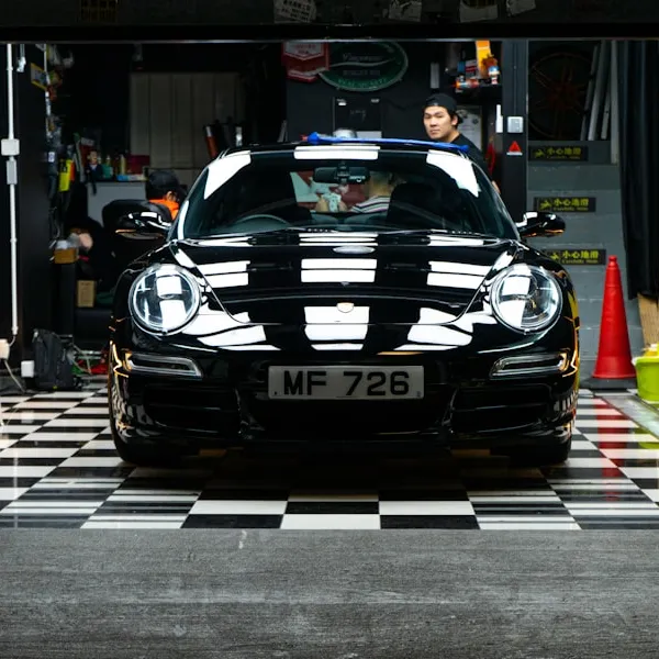 Frente, faros y parabrisas de un Porsche negro en un taller; fotografía de referencia.